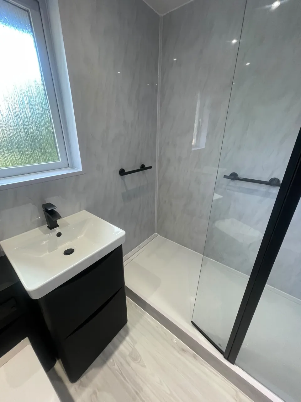 Black vanity and glass shower screen with pale walls
