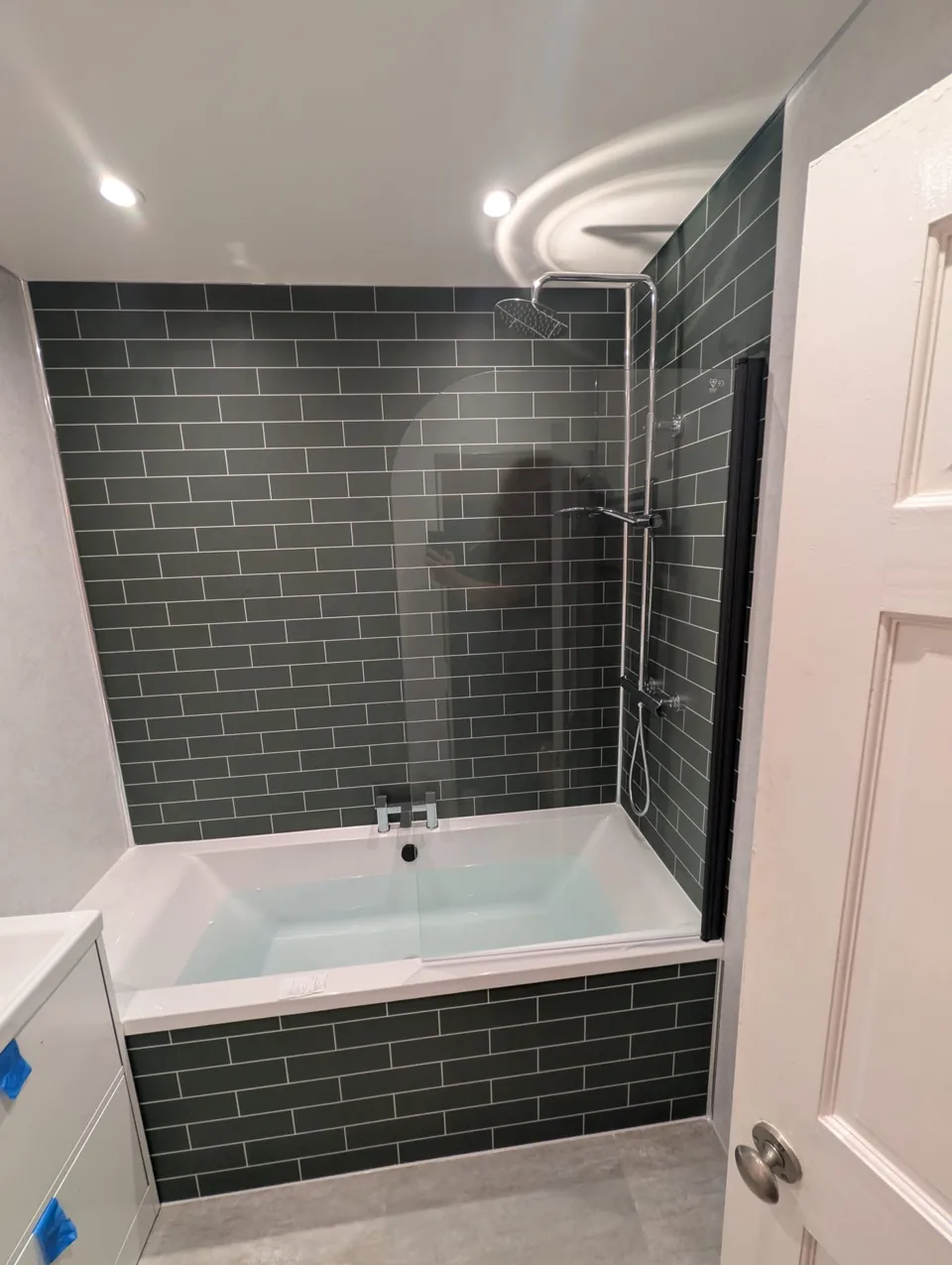 Fitted bath with green tiles and white bathroom furniture
